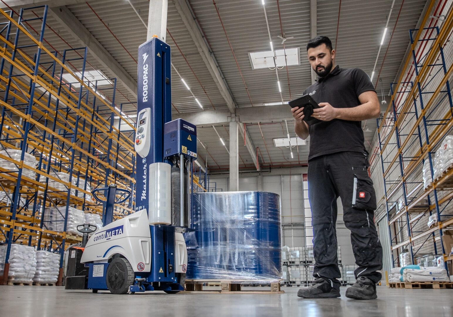 Imagefilm Industriefotografie für Nelo Neuss Logistik, die einen Lagerist in Arbeitskleidung im modernen Lager mit Packroboter zeigt