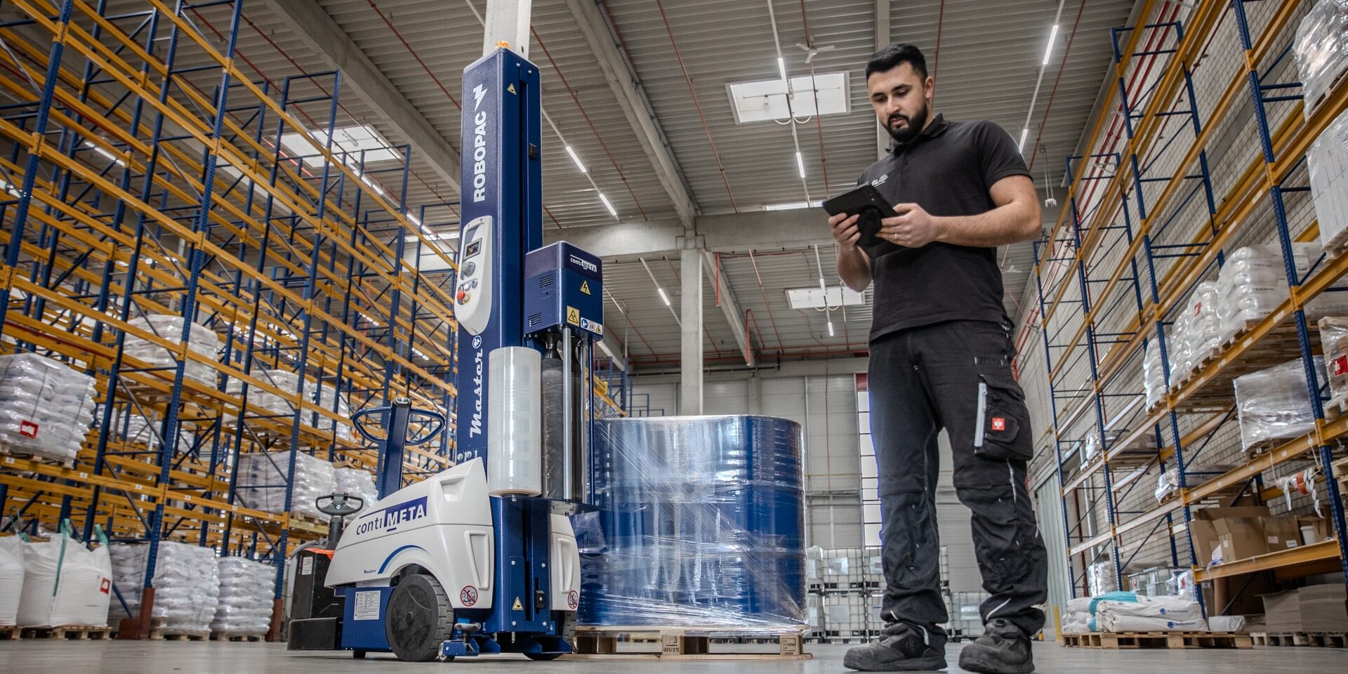 Imagefilm Industriefotografie für Nelo Neuss Logistik, die einen Lagerist in Arbeitskleidung im modernen Lager mit Packroboter zeigt